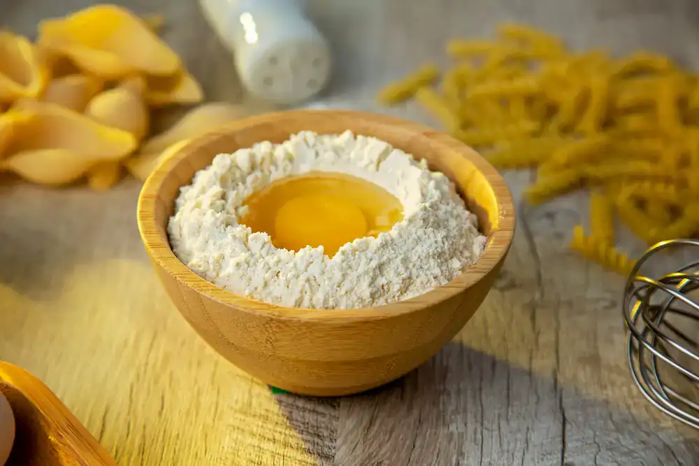 Traditional pasta making tools, a mound of semolina flour, and fresh egg yolks