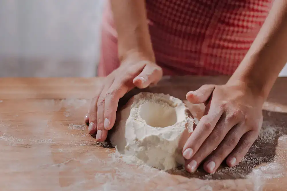 Artisan hands kneading fresh pasta dough on a floured wooden surface